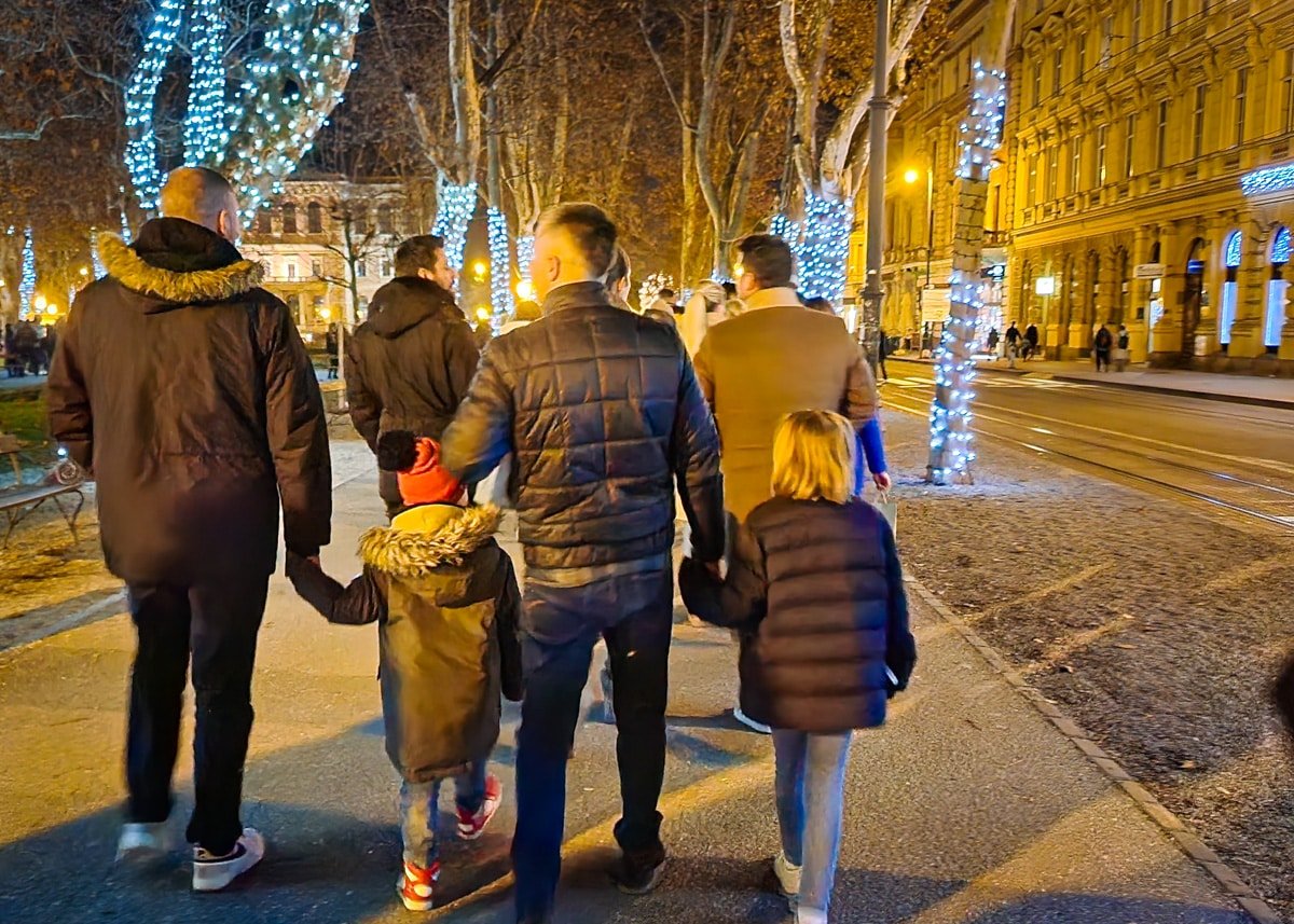 A group of people walking down a street adorned with festive Christmas lights during Advent in Zagreb.