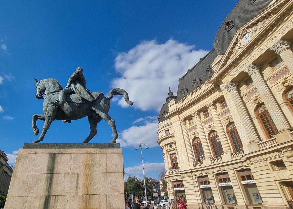 A statue of a man riding a horse in front of a building at Revolution Square - Bucharest.