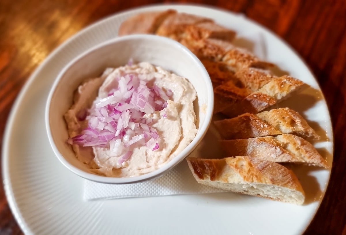A bowl of dip with bread and onion on a plate at Caru' cu Bere Bucharest. 