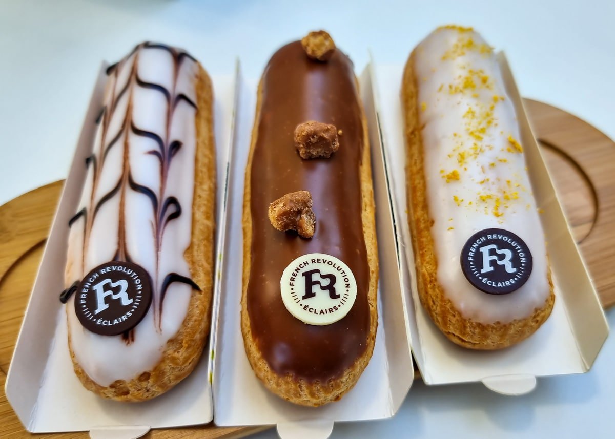 Three different types of eclairs are sitting on a tray at French Revolution Eclairs.