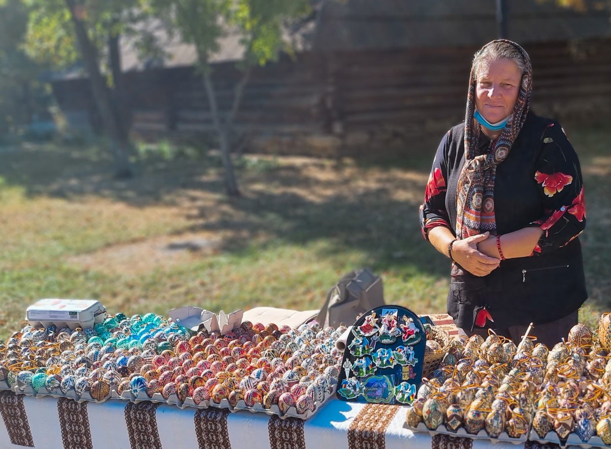 A woman is standing next to a table full of Romanian Easter Eggs in the Dimitrie Gusti National Village Museum
