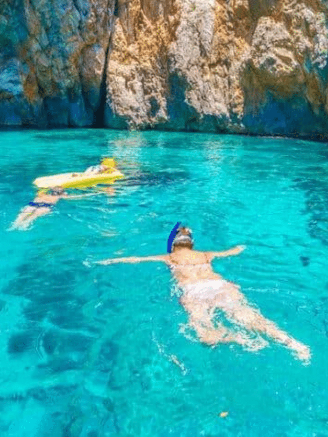 Two people swimming in the clear blue water near a cliff in the picturesque Pakleni Islands.