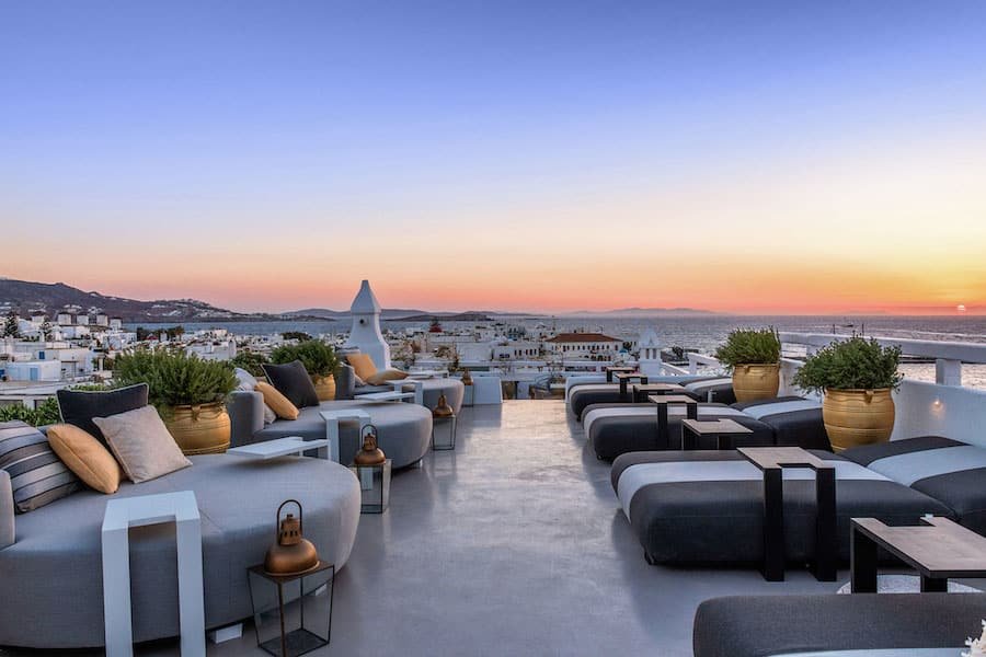 A rooftop terrace with lounge chairs and a view of the sea, perfect for enjoying the summer in Mykonos.
