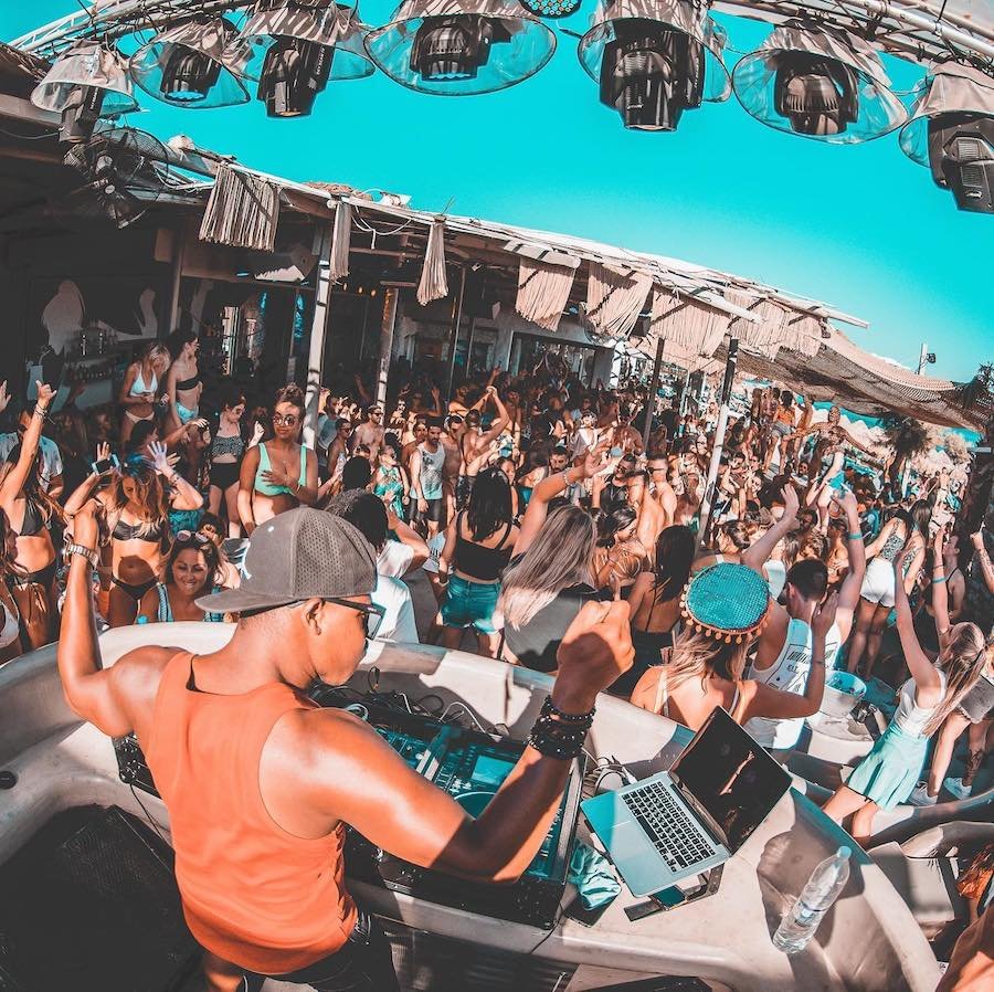 A group of people at a Mykonos beach party with summer vibes and lively DJs at beach clubs.