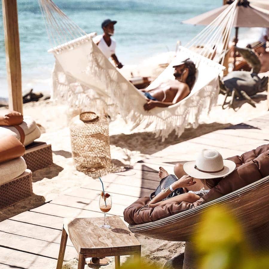 A group of people enjoying a summer retreat on the beach, relaxing in hammocks at one of the popular beach clubs in Mykonos.