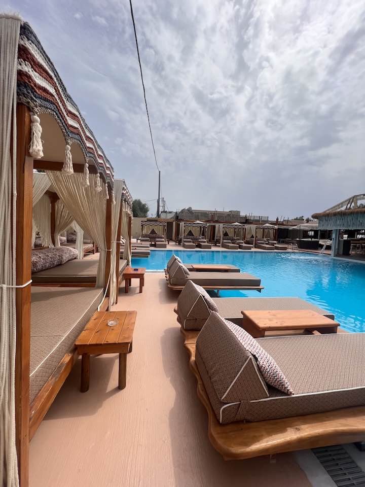 A Santorini beach club featuring a swimming pool adorned with lounge chairs and umbrellas - JoJo’s Beach Bar Santorini