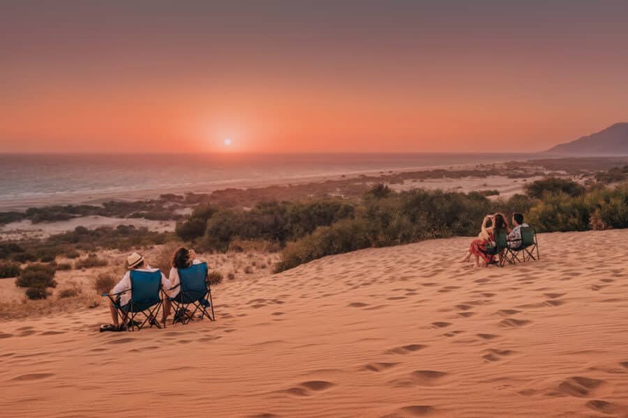 Patara, Turkey: group of travelers sit on camping chairs and enjoy and watch the stunning sunset over the sand dunes of Patara beach, Antalya