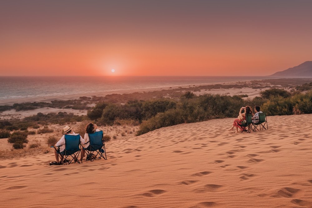 Patara, Turkey: group of travelers sit on camping chairs and enjoy and watch the stunning sunset over the sand dunes of Patara beach, Antalya