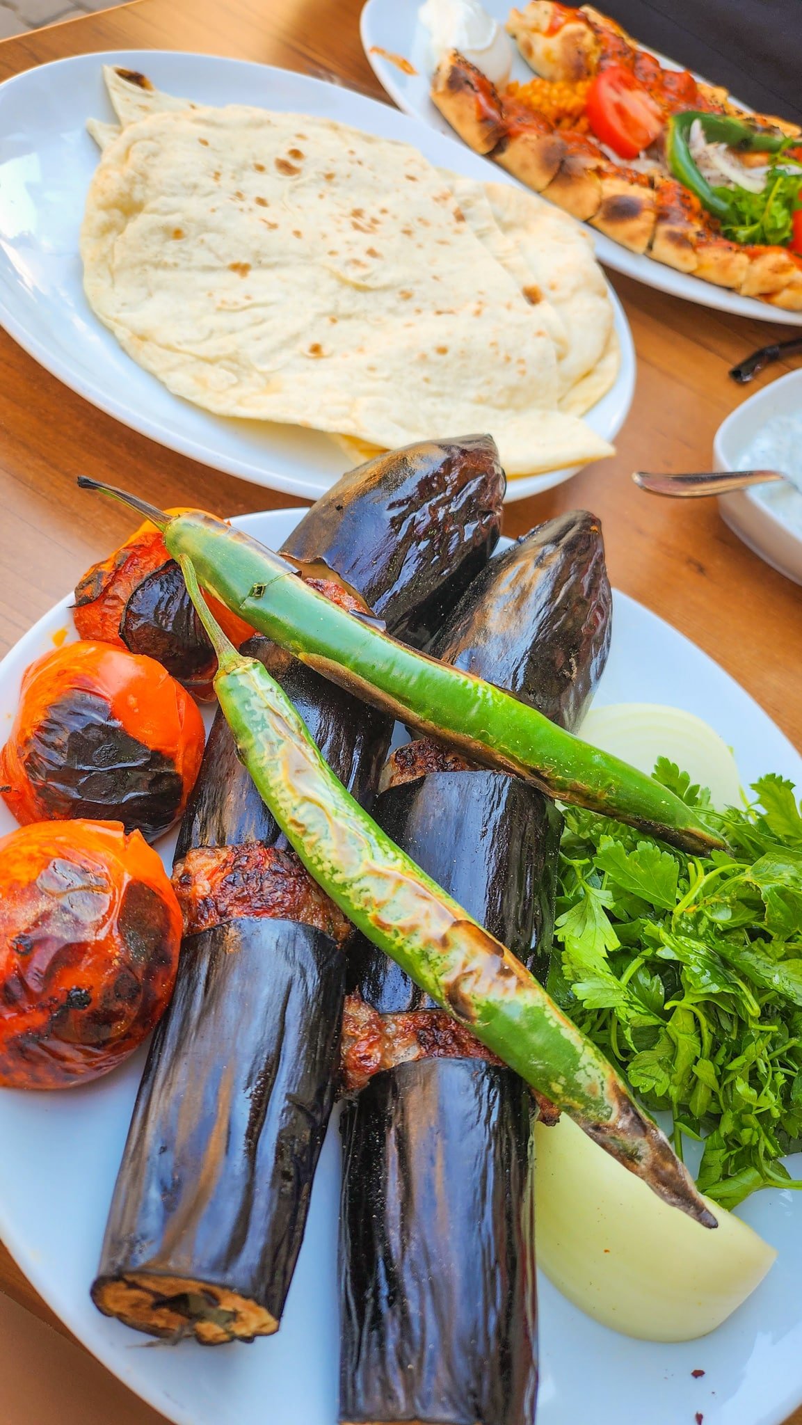 Grilled eggplants, tomatoes, green chilies, and a whole onion, served with fresh herbs and flatbread on wooden tables alongside the best Turkish kebabs.