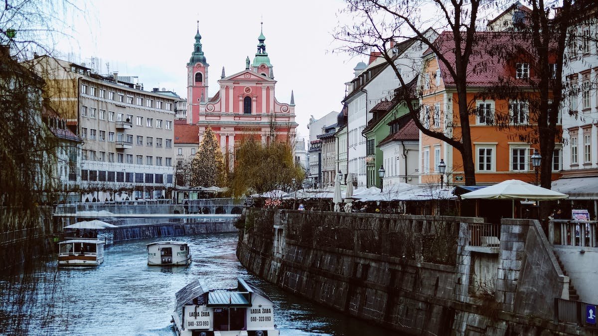 A picturesque canal in Ljubljana with boats leisurely gliding along, framed by charming buildings in the background.