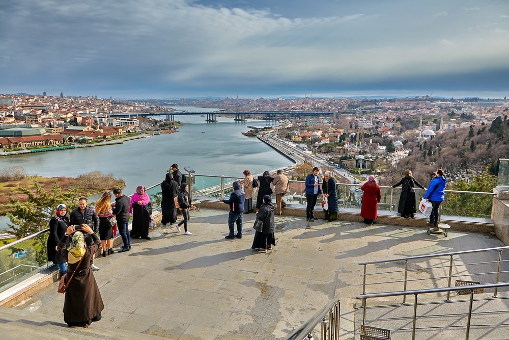 A group of people standing on a balcony overlooking the Istanbul river, enjoying the best view from Pierre Loti Hill