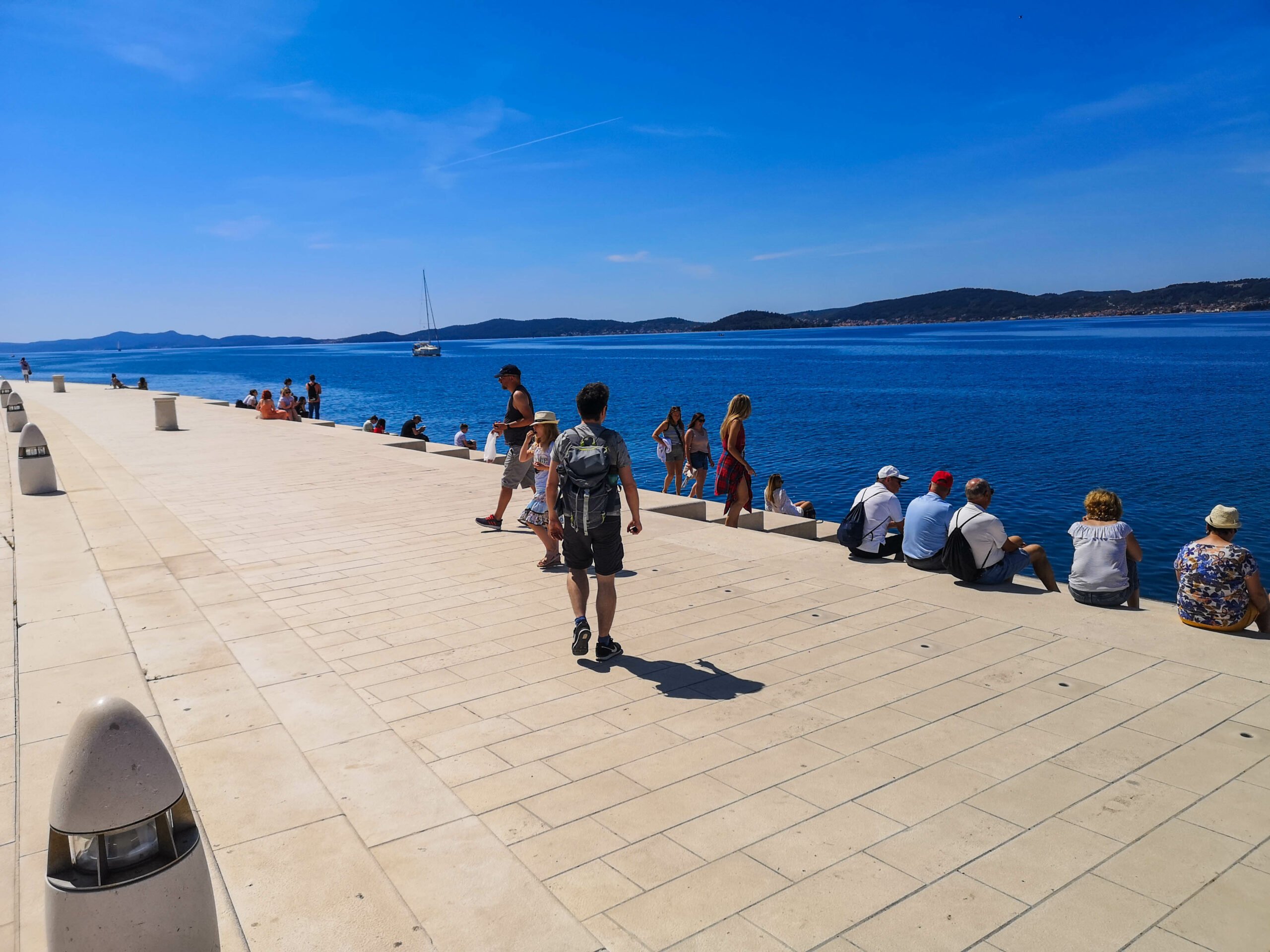 A group of people standing on a pier near the water next to the Zadar Sea Organ