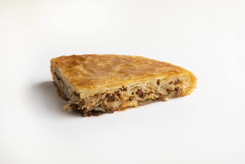 A slice of burek minced meat, a delectable example of Bosnian foods, presented on a plain white background.