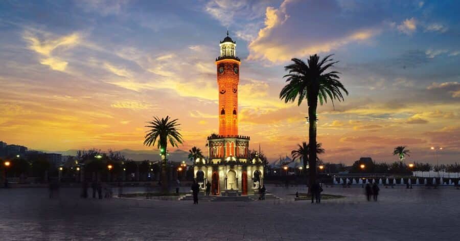 A clock tower in a plaza is lit up at dusk, creating a captivating sight for Izmir nightlife enthusiasts.