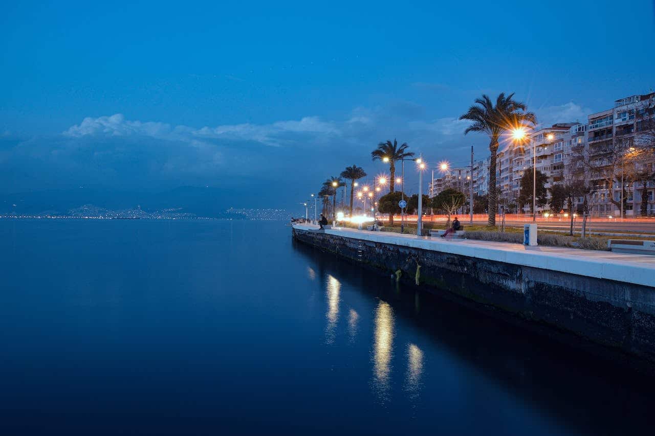 A pier with palm trees along the water at dusk, offering a beautiful setting for Izmir nightlife and things to do. PLS GET READY for an unforgettable evening.