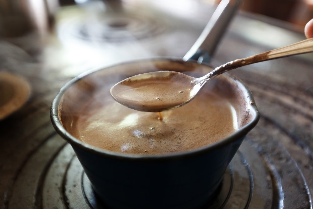 The best Turkish coffee, brewed to perfection, is being stirred with a small spoon in a traditional copper pot.