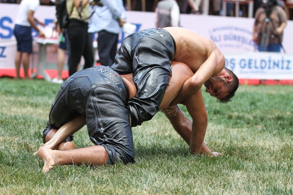 Two men engaging in Turkish wrestling on the grass in front of a crowd.