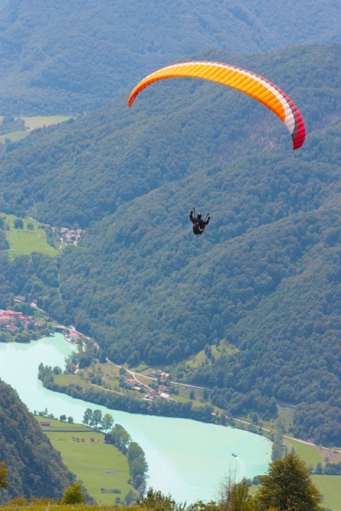 A person is paragliding over the Soča River Valley.