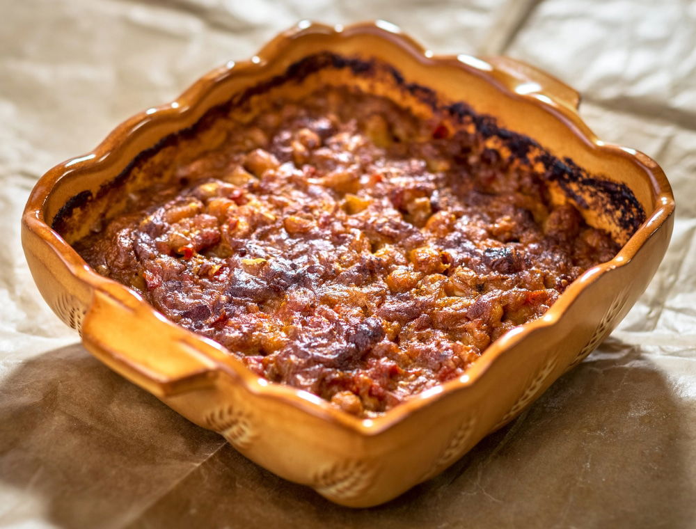 A brown ceramic dish filled with a baked Prebranac, a comforting Bosnian food, placed on a sheet of parchment paper.