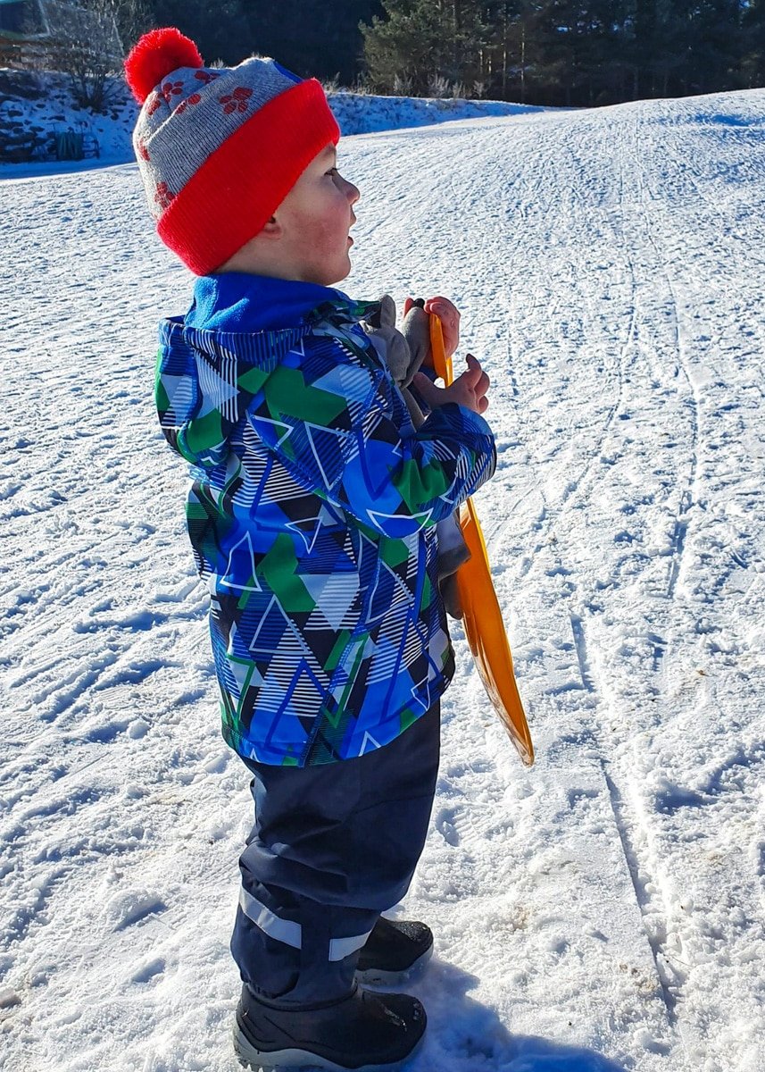 A young boy standing in the snow with a ski pole.
