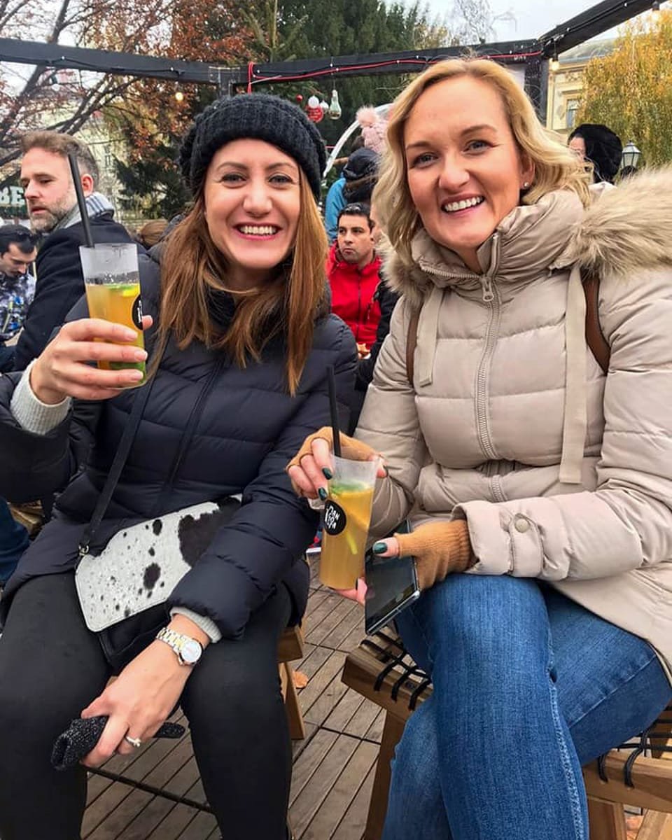 Two women sitting on a wooden bench with drinks in their hands.