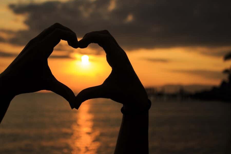 A person's hands create a heart shape at sunset while enjoying the vibrant Izmir nightlife.