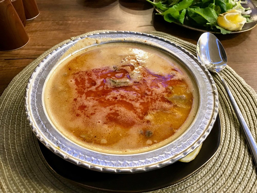 Is a bowl of Turkish Soup Beyran with Lamb Meat, Rice, Chopped Garlic and Vinegar Sauce Served with Salad. 