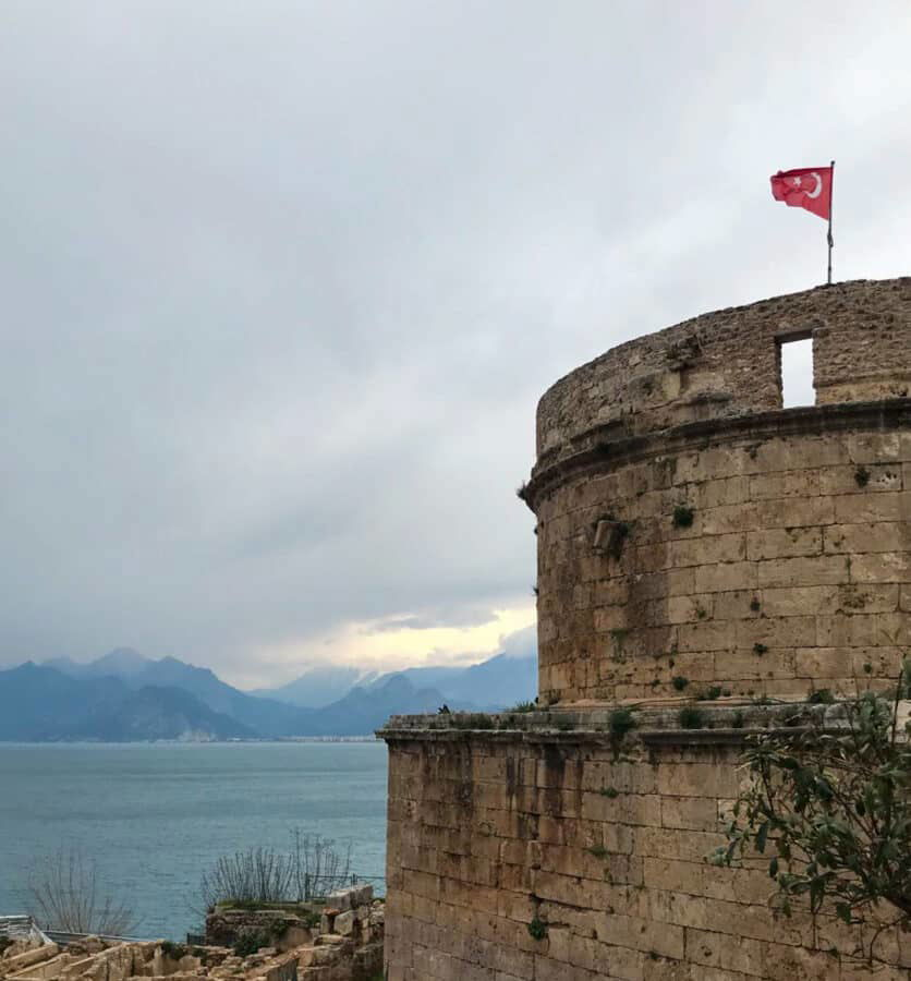 Antalya castle - stone tower with a flag on top of it.