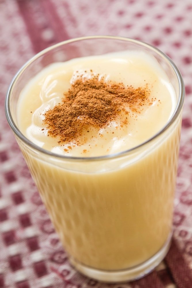 A glass of creamy beverage topped with a sprinkle of cinnamon, served on a patterned tablecloth - Boza or Bosa, traditional Turkish dessert