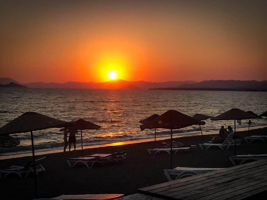 The sun is setting over Calis Beach with chairs and umbrellas.