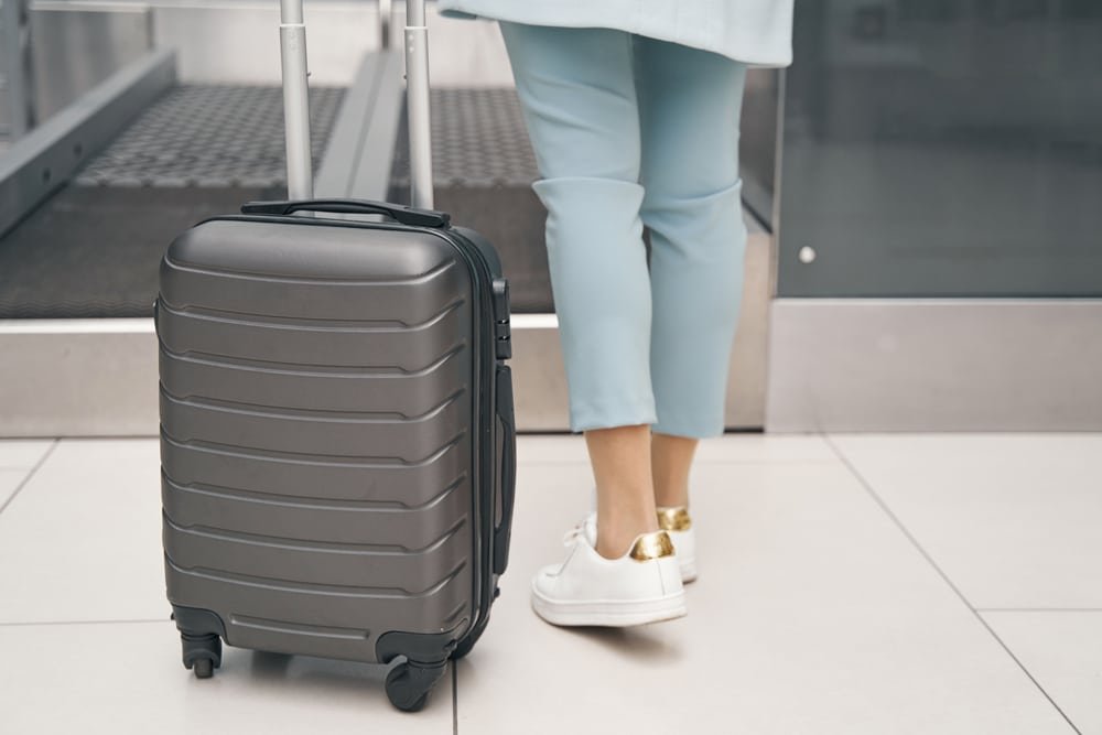 Woman standing with a suitcase at an airport, wearing comfy shoes for travel.