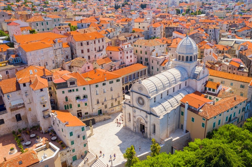 Aerial view of a historic cathedral surrounded by tightly packed buildings with red roofs in a Croatian old town.