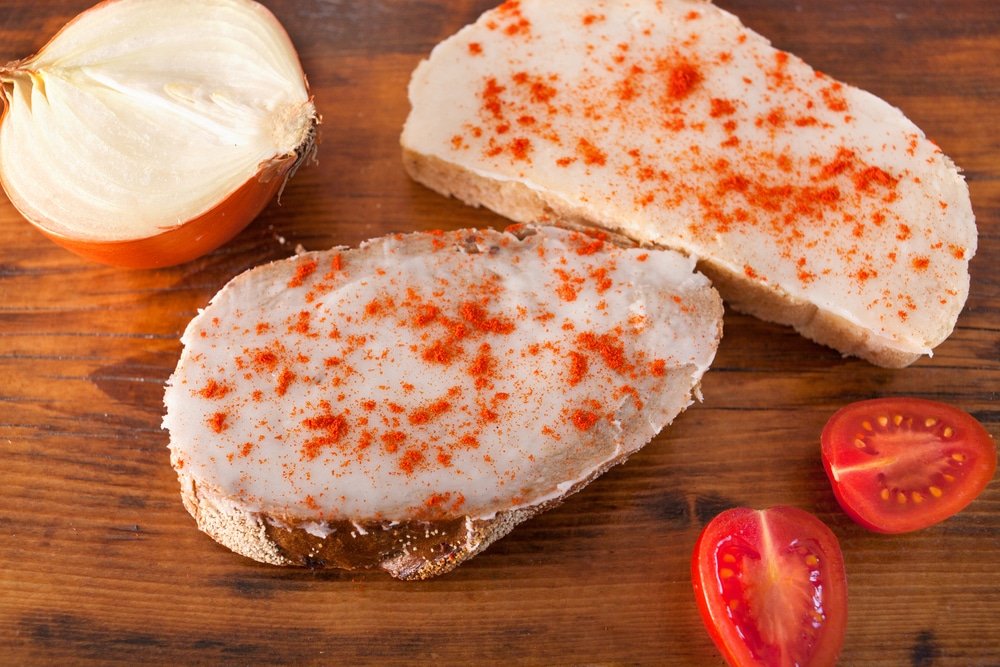 Weird food in Croatia. Slices of bread spread with lard and sprinkled with paprika, accompanied by onion and tomato slices on a wooden board - Kruh, Mast i Paprika (Bread, Lard, And Paprika)