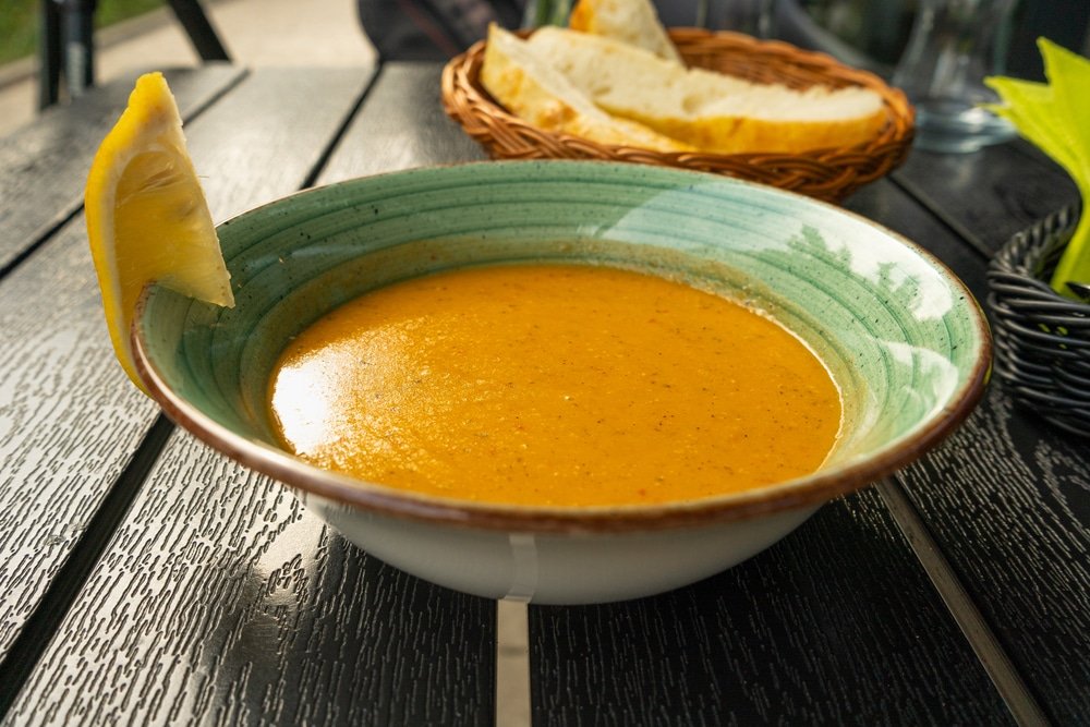 A bowl of Mercimek Çorbası soup next to a basket of bread on a table in Turkey.
