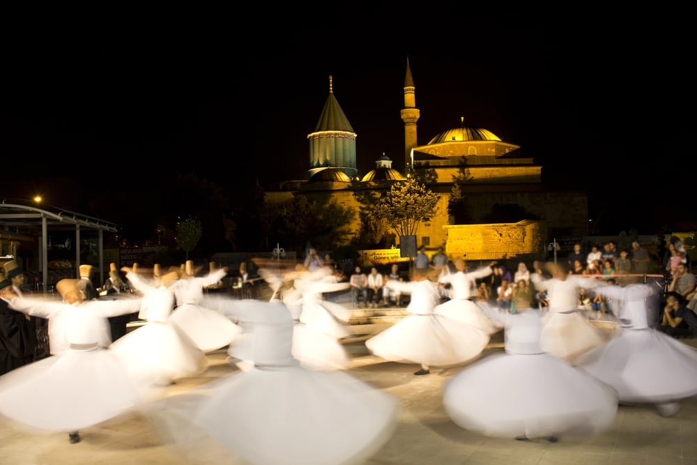 A group of Whirling Dervishes, dancing in front of a building in Konya.