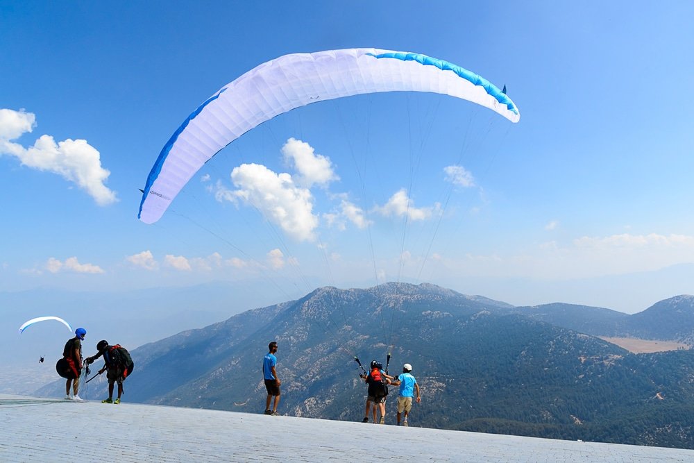 A group of people standing on top of Babadag Mountain with a paraglider, overlooking the breathtaking natural attractions in Turkey.