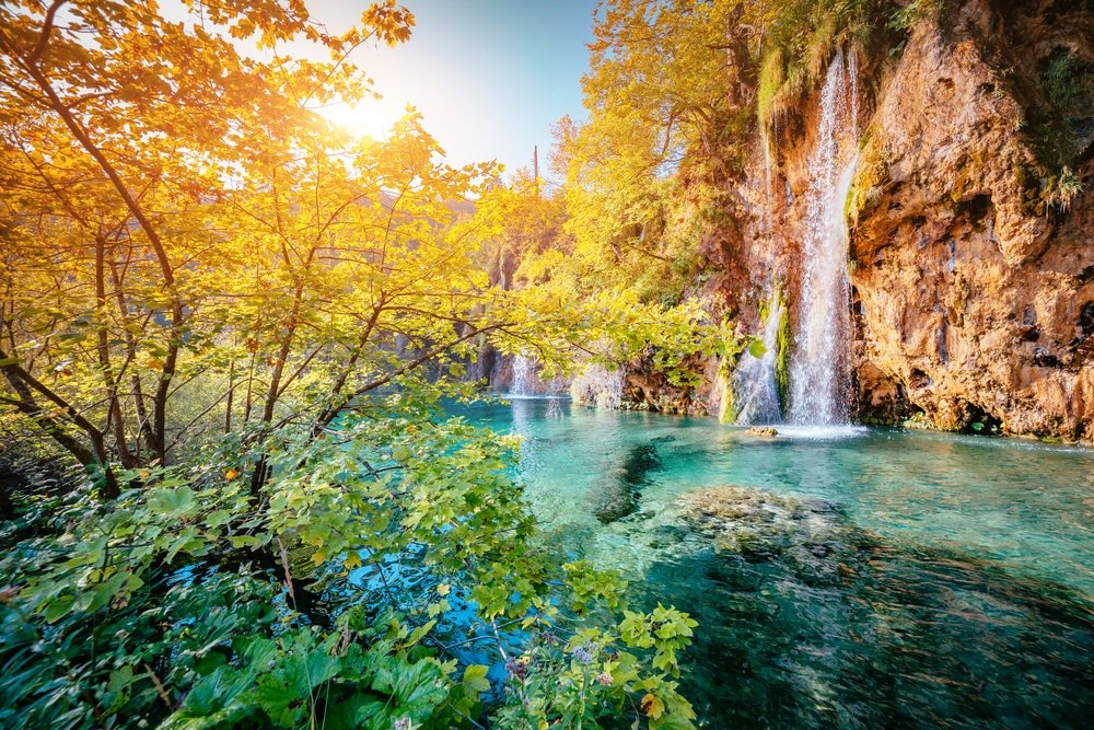 Is Plitvice Lakes worth visiting? Autumn at Plitvice Lakes reveals a tranquil waterfall with lush foliage in a serene forest setting, highlighting why the destination is truly worth visiting.
