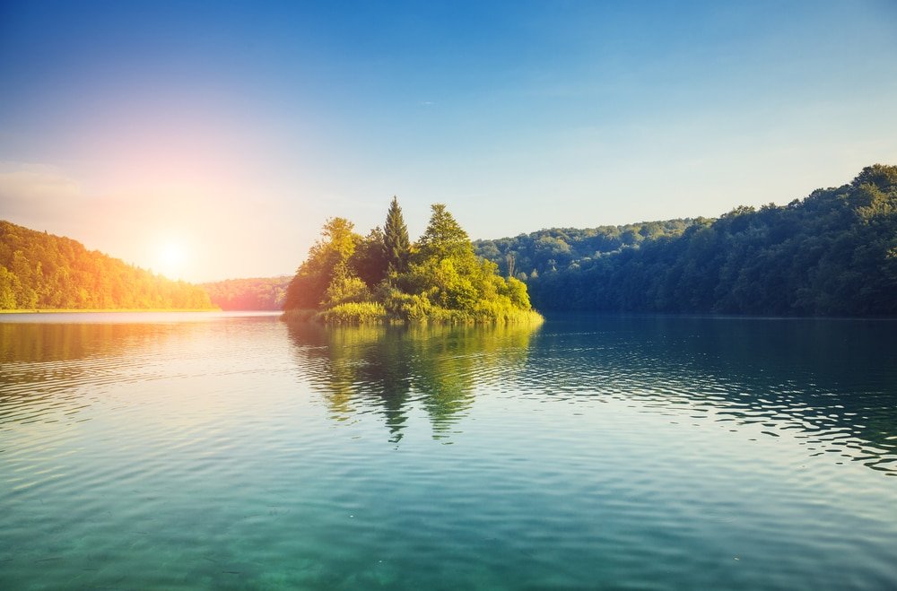 Sunrise over a tranquil lake with a small forested island in the center of Plitvice Lakes.