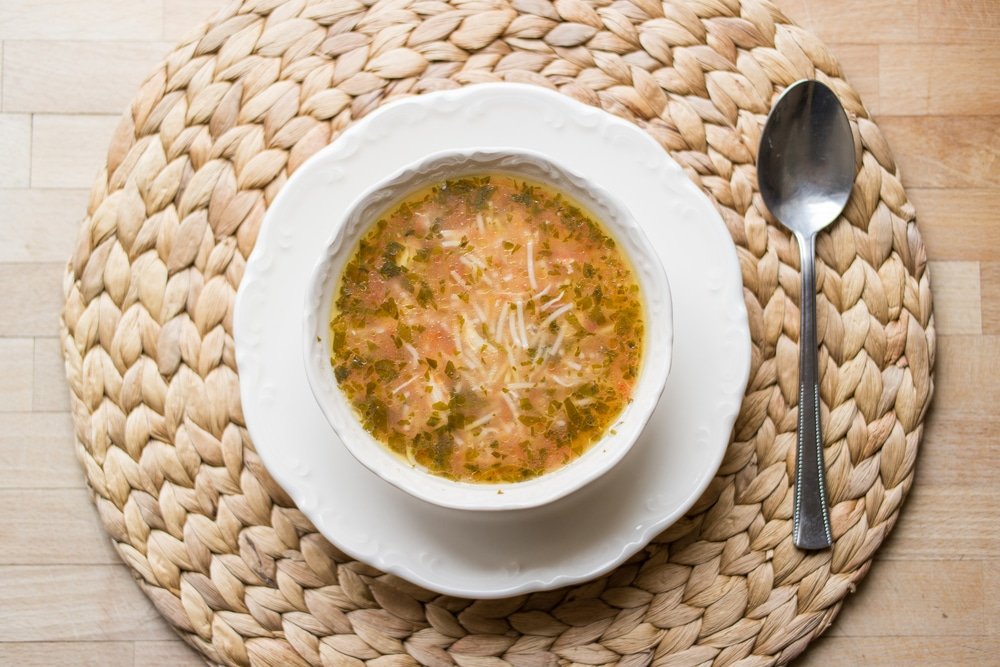 A bowl of Tavuk Suyu Çorbas soup with a spoon on a woven mat, popular in Turkey.
