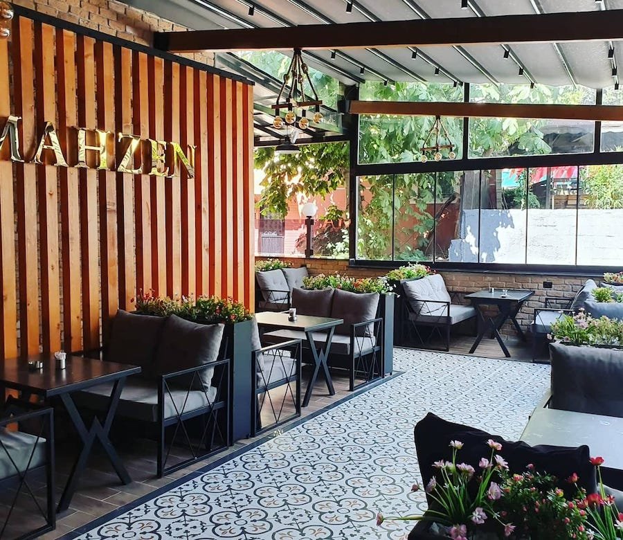 A stylish outdoor seating area of a cafe with patterned flooring, comfortable furniture, decorative plants, and hookahs in Istanbul.