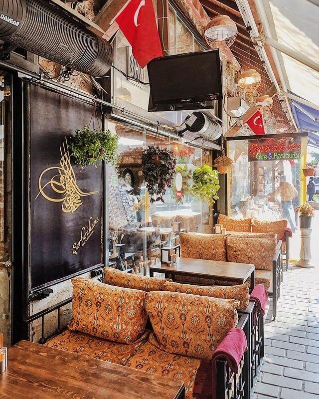 Outdoor seating at a quaint cafe with patterned cushions and Turkish flags, exuding a cozy and traditional ambiance, completes the setting with hookah available in Istanbul.