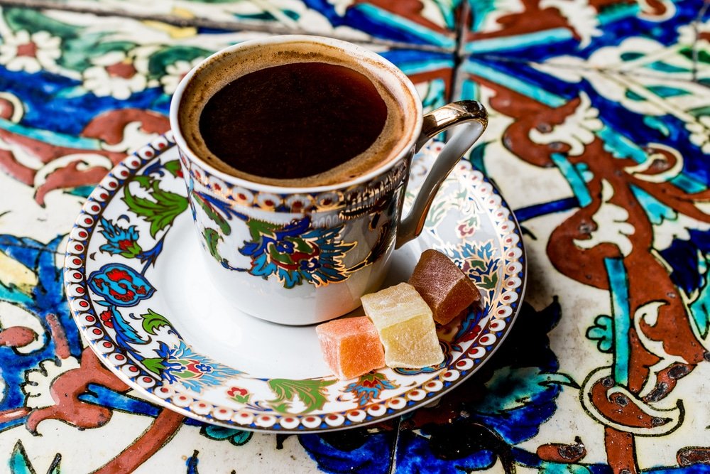 A cup of Turkish coffee is sitting on a saucer on a colorful tiled floor.