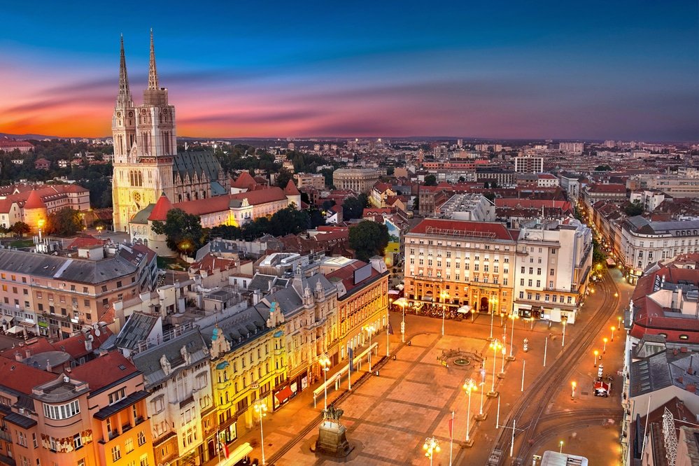 Aerial view of a city square and surrounding architecture in Croatia at dusk with vibrant sunset colors in the sky.