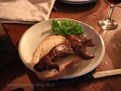 A grilled dormous served on a slice of bread with a lettuce garnish on a white plate, showcasing weird Croatian food.