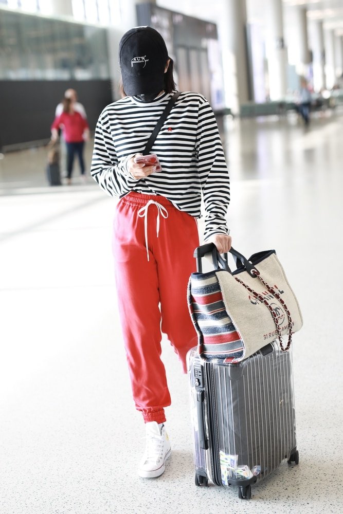 Person in striped shirt and red pants, embodying the "Be Comfy on a plane" look while pulling a suitcase in an airport terminal.