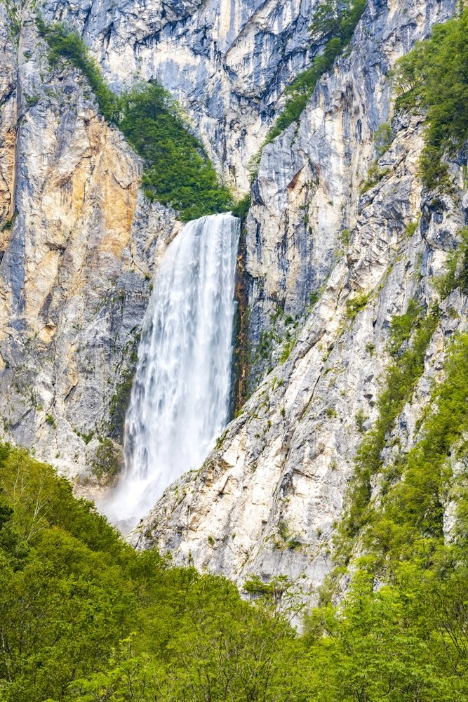 Boka waterfall, one of the best waterfalls in Slovenia, cascades down a rugged cliff surrounded by lush green foliage.