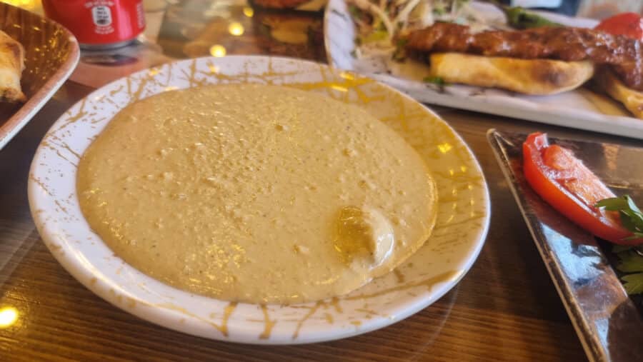 A bowl of smooth, creamy hummus with a dollop of olive oil in the center, served on a table in Goreme with various other dishes in the background.