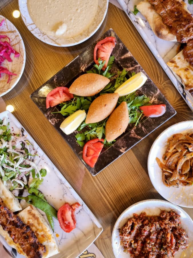 Overhead view of a middle eastern meal in Goreme featuring kibbeh, skewered meats, hummus, onions, and tomatoes on a table.