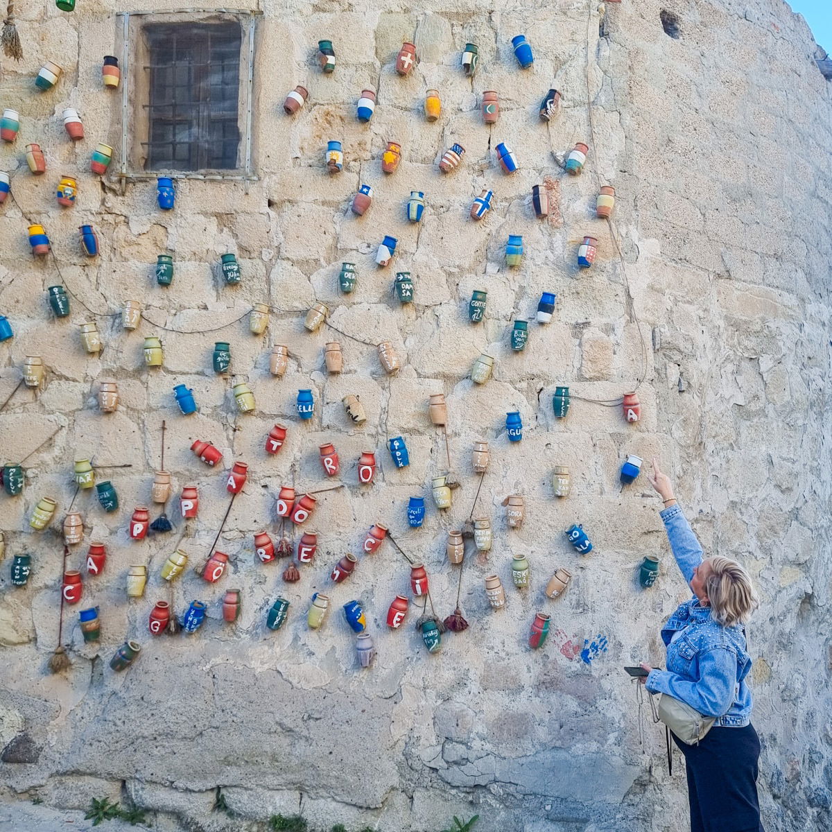 Sj paints on an old wall adorned with colorful hanging tin cans in an outdoor urban art project in Goreme, Cappadocia.
