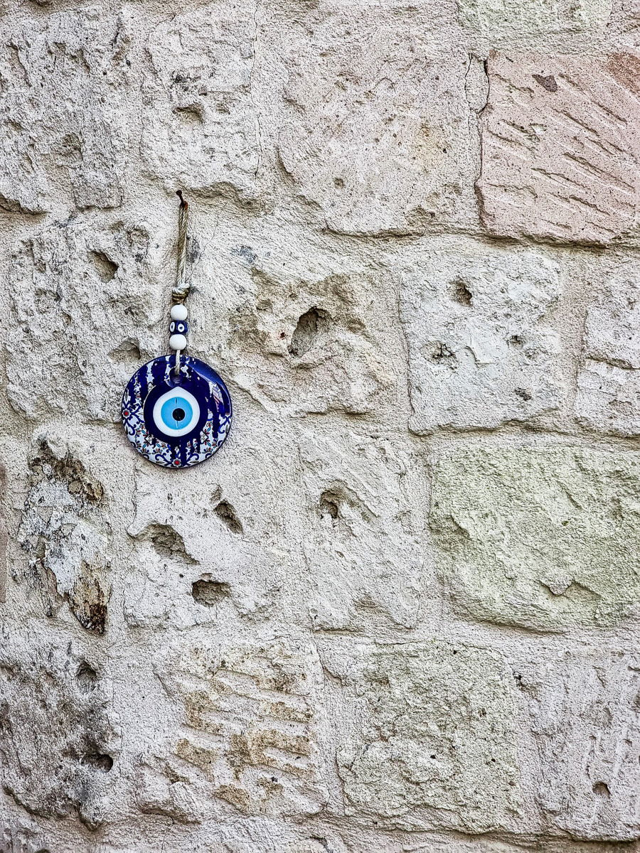 Blue and white evil eye amulet hanging on a rough, textured stone wall in Goreme, Cappadocia.
